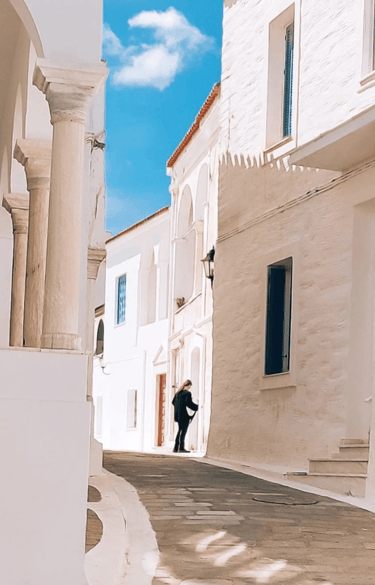 A person walking through a bright whitewashed Cycladic alley