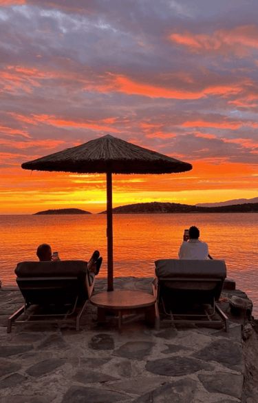 Two people watching the sunset under a straw umbrella