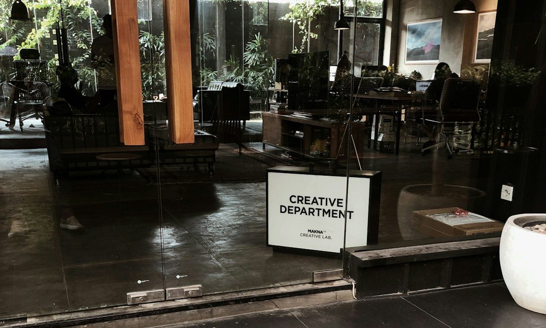 The glass frontage of a creative studio at street level, with a lit sign and people working at desks inside