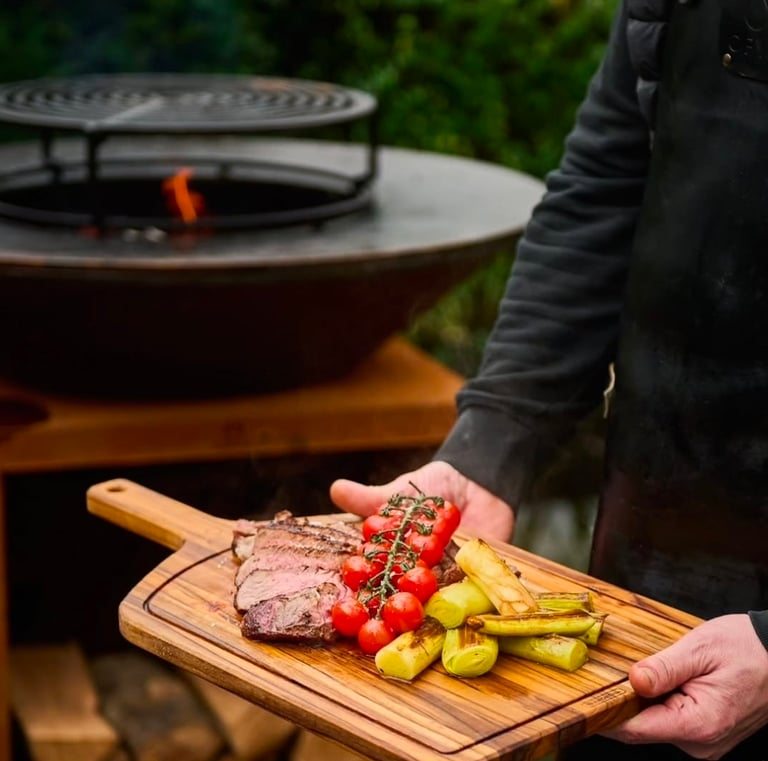 Bistecca e verdure grigliate su un tagliere di legno accanto a un braciere